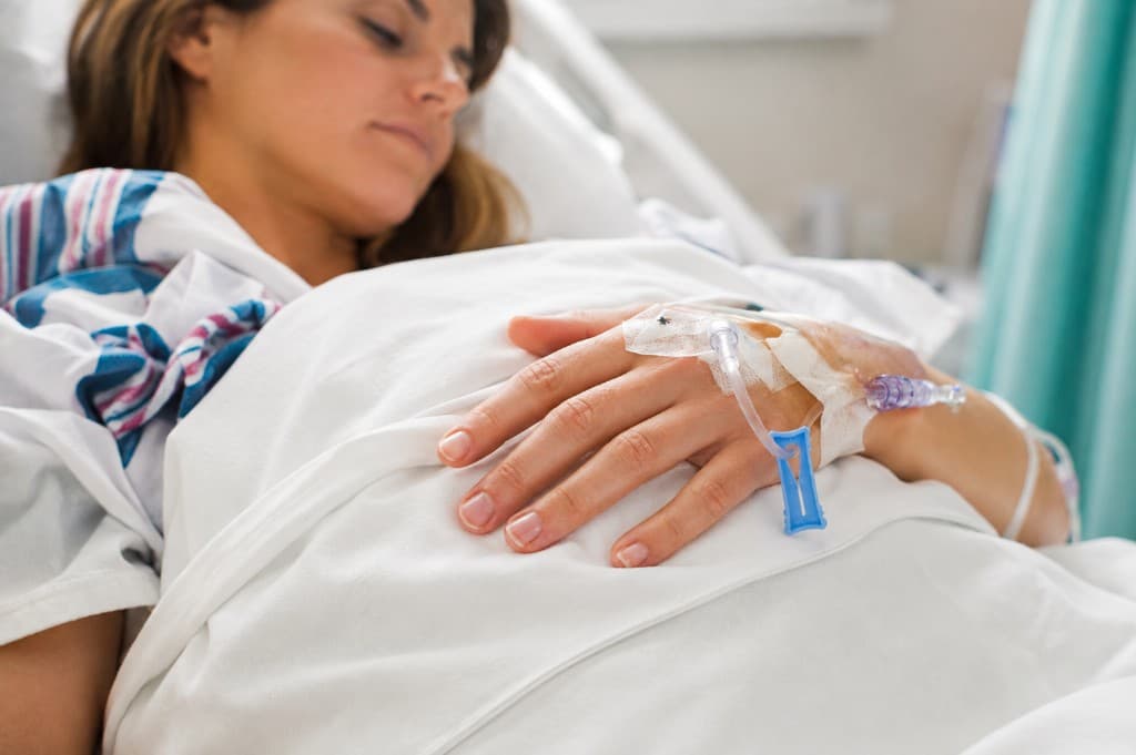 Patientin ruht im Klinikbett, Infusion an der Hand